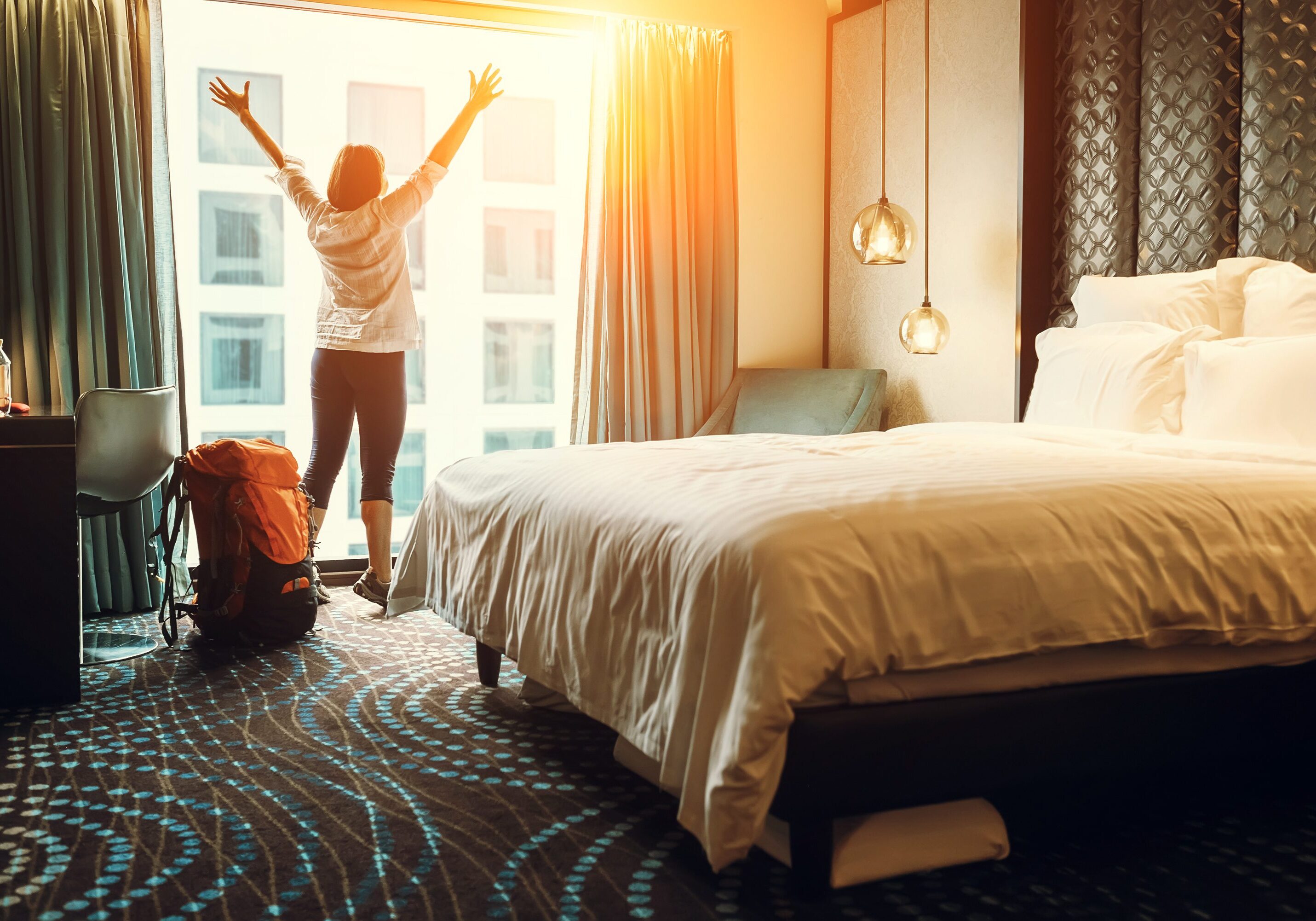 Person stretching in a sunlit hotel room near a large window.