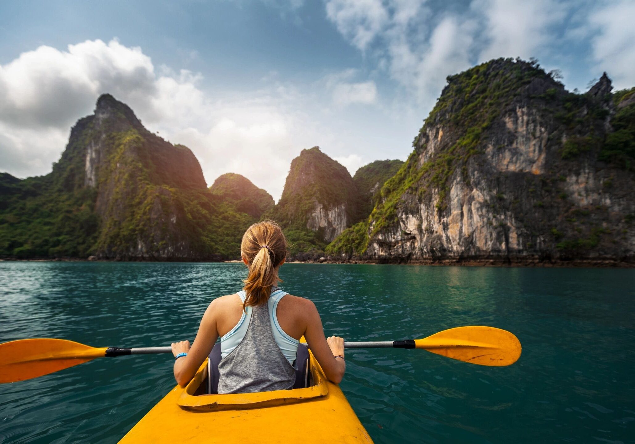 A woman kayaking in clear blue waters surrounded by towering cliffs.